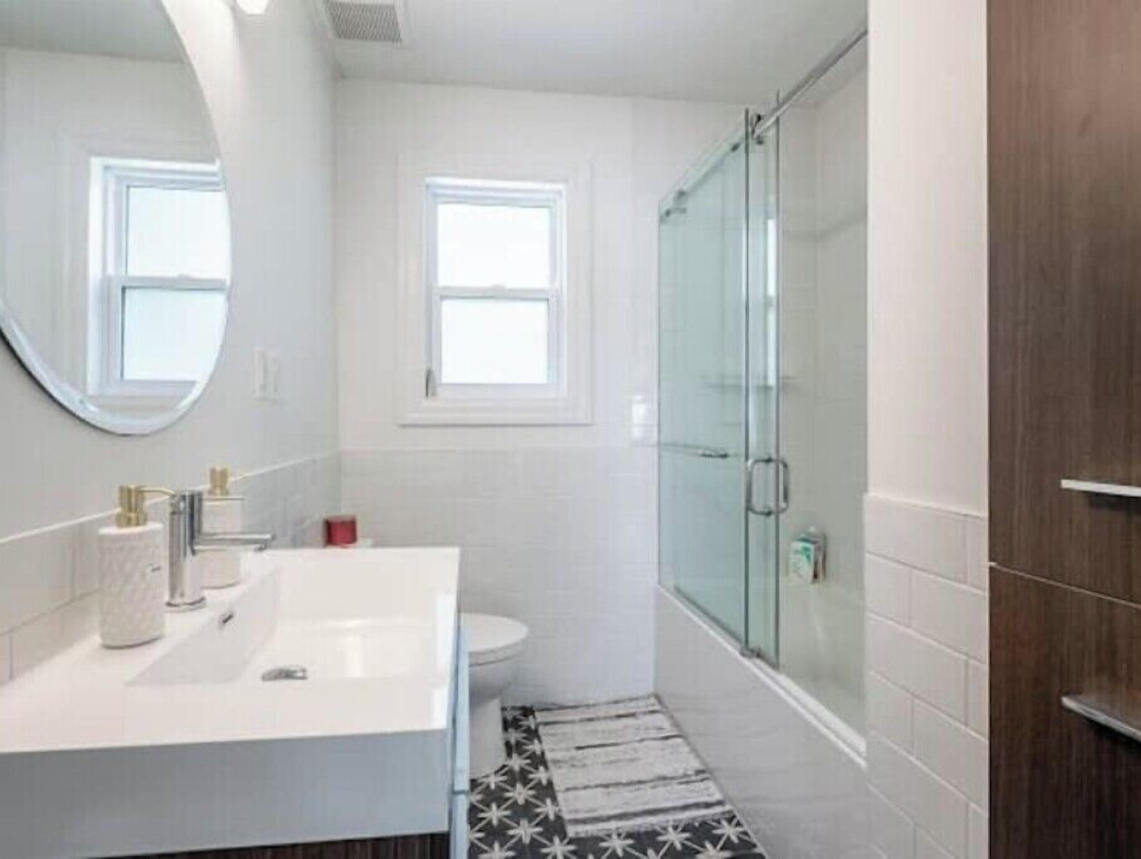 Een moderne badkamer met een wit wastafelmeubel, een glazen douchecabine en een klein raam.