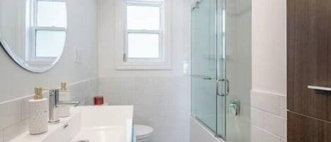 Een moderne badkamer met een wit wastafelmeubel, een glazen douchecabine en een klein raam.