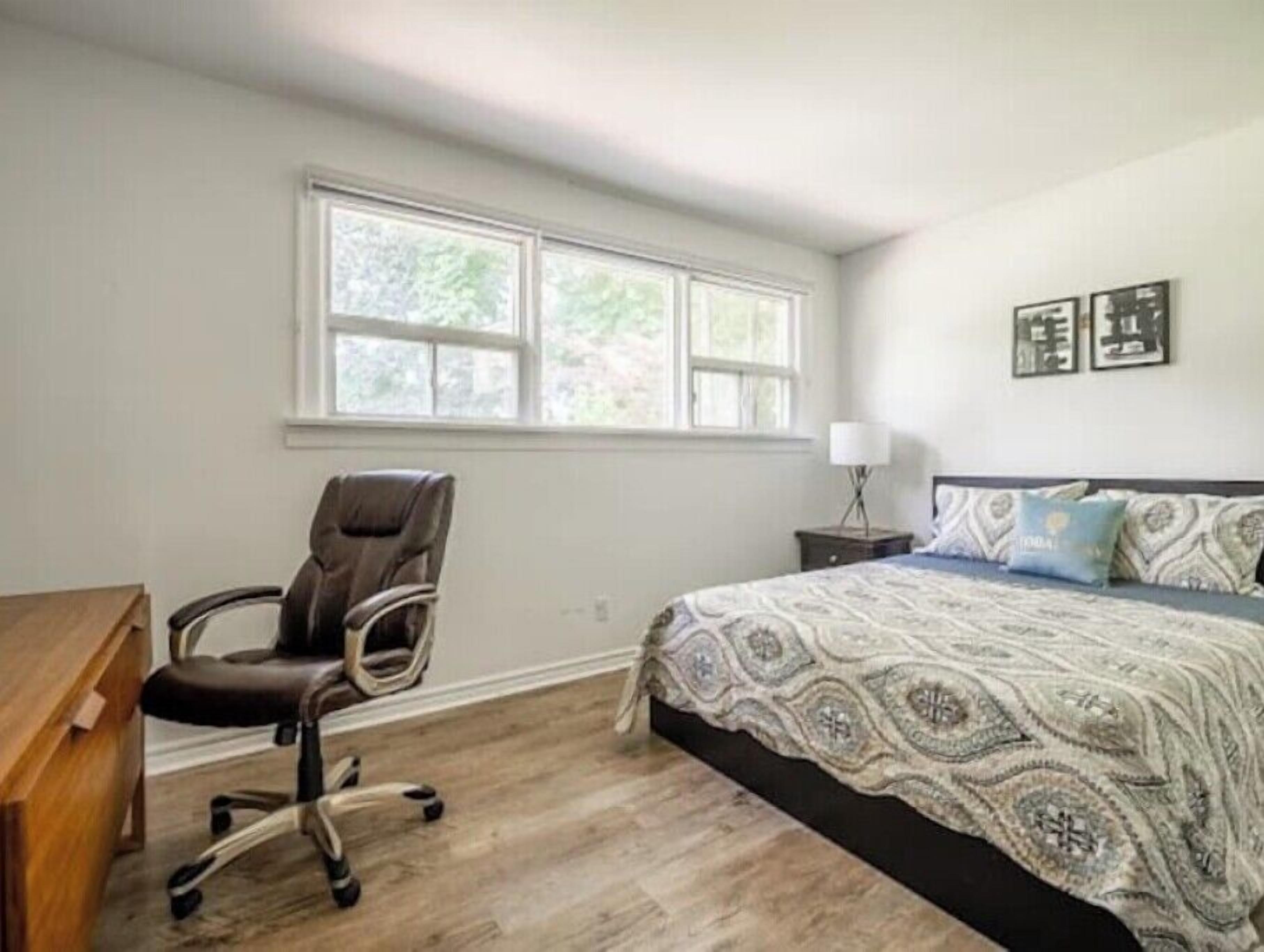 A bedroom with a large bed, a desk, a chair, and a window.