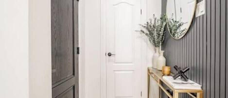 A hallway with a white door, a console table with vases, and a mirror on the wall.