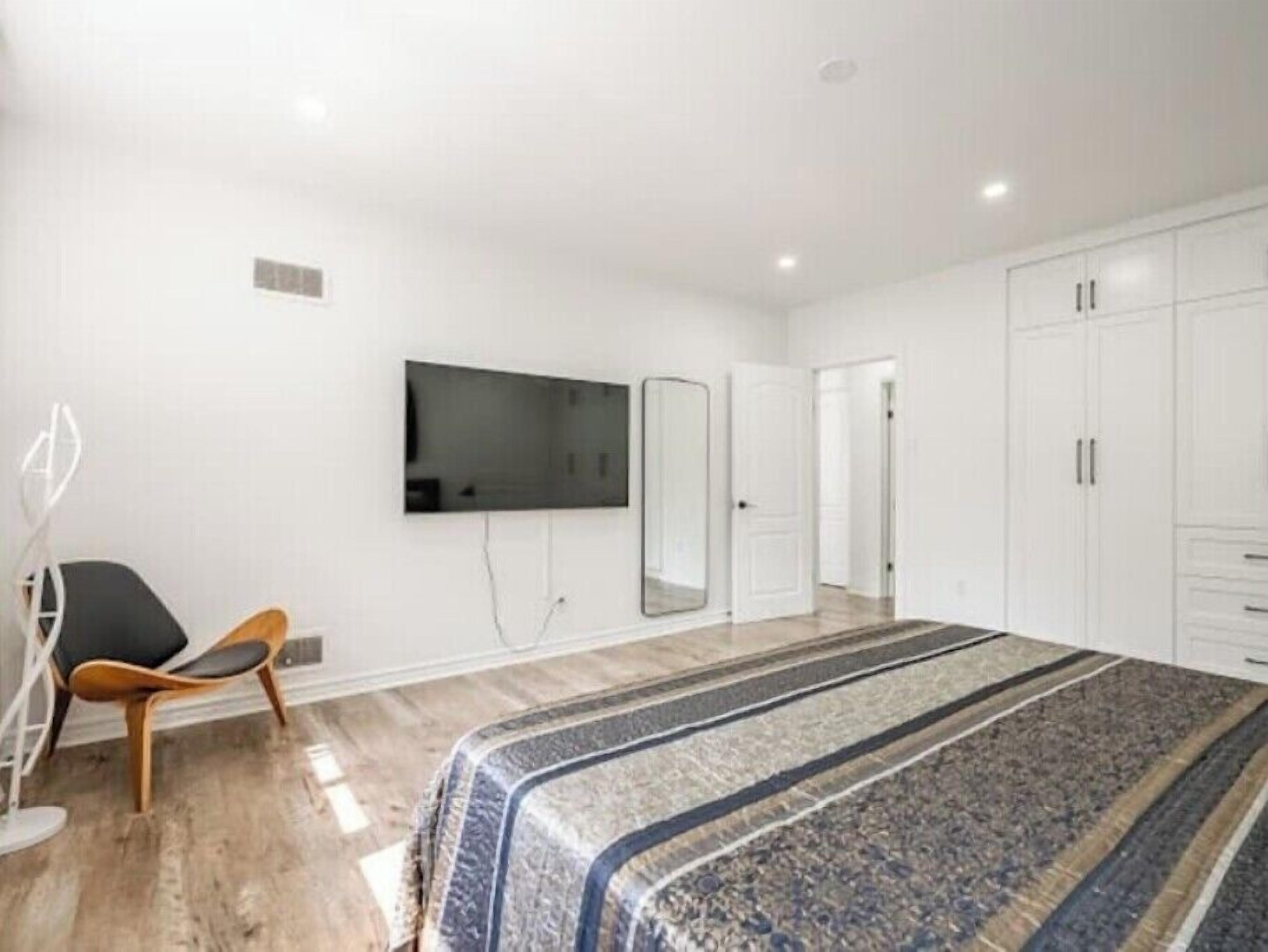 Une chambre avec un lit, une chaise, un téléviseur fixé au mur et des armoires blanches.
