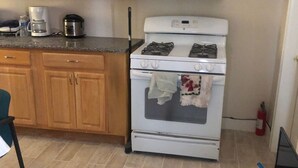 Een keuken met houten kastjes, een witte kookplaat, een koffiezetapparaat en een laptop op een tafel.