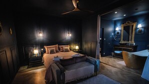 A dark-themed bedroom with a bed, bedside lamps, a vanity with a mirror, and a bathtub. - Ideal for friends: "La Belle Dame sans Regrets" with swimming pool, garden & workshop  (Talairan)
