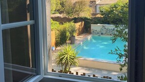 A view from a window of a swimming pool surrounded by greenery and stone walls. - Ideal for friends: "La Belle Dame sans Regrets" with swimming pool, garden & workshop  (Talairan)