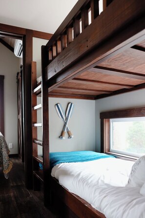 Una cama individual con estructura de madera, una ventana con vistas y dos palos de hockey colgados en la pared.