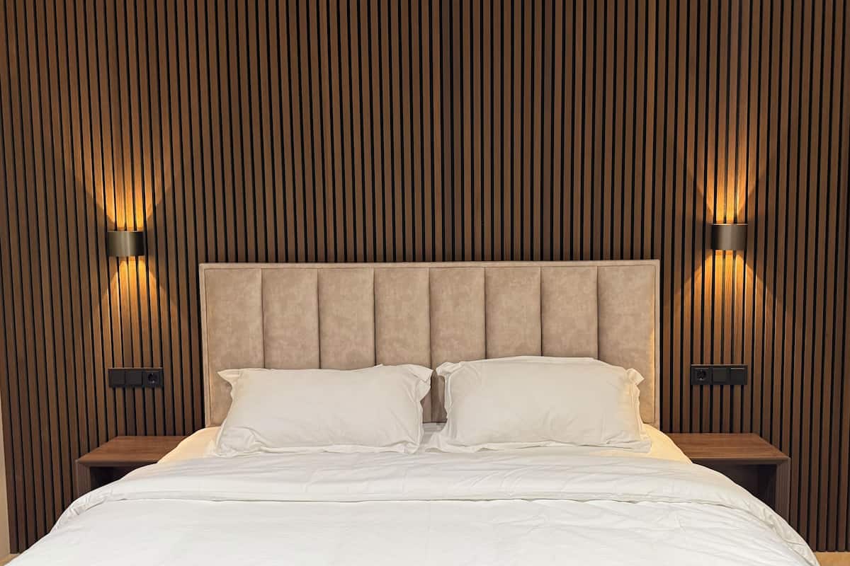A bed with a padded headboard, two bedside tables, and wall-mounted lighting.