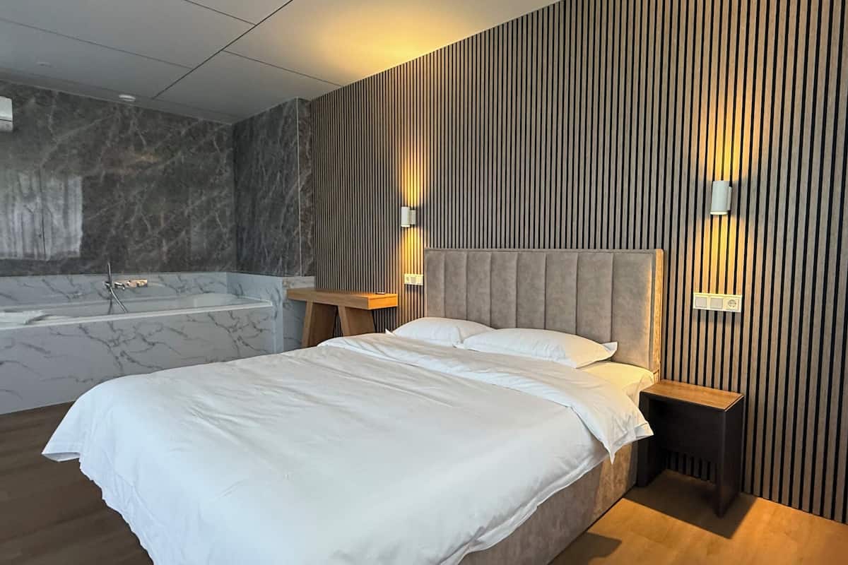 A modern bedroom with a large bed, a built-in bathtub, and wooden paneling on the walls.