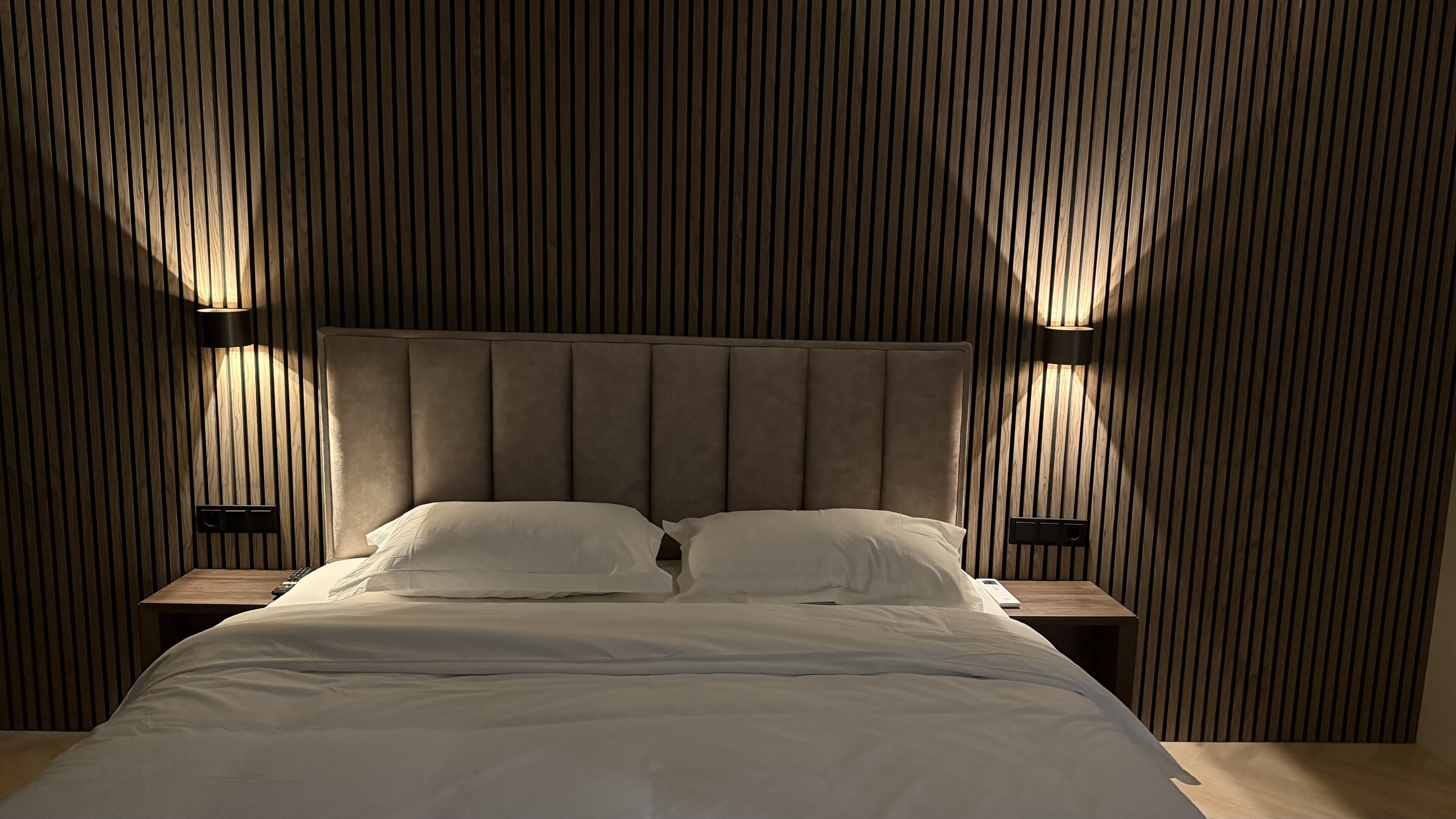 Un dormitorio con una cama grande, dos mesitas de noche y un cabecero de listones de madera.