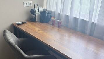 A room with a wooden desk, a black coffee maker, two plaid cups, a remote control, and a grey chair.