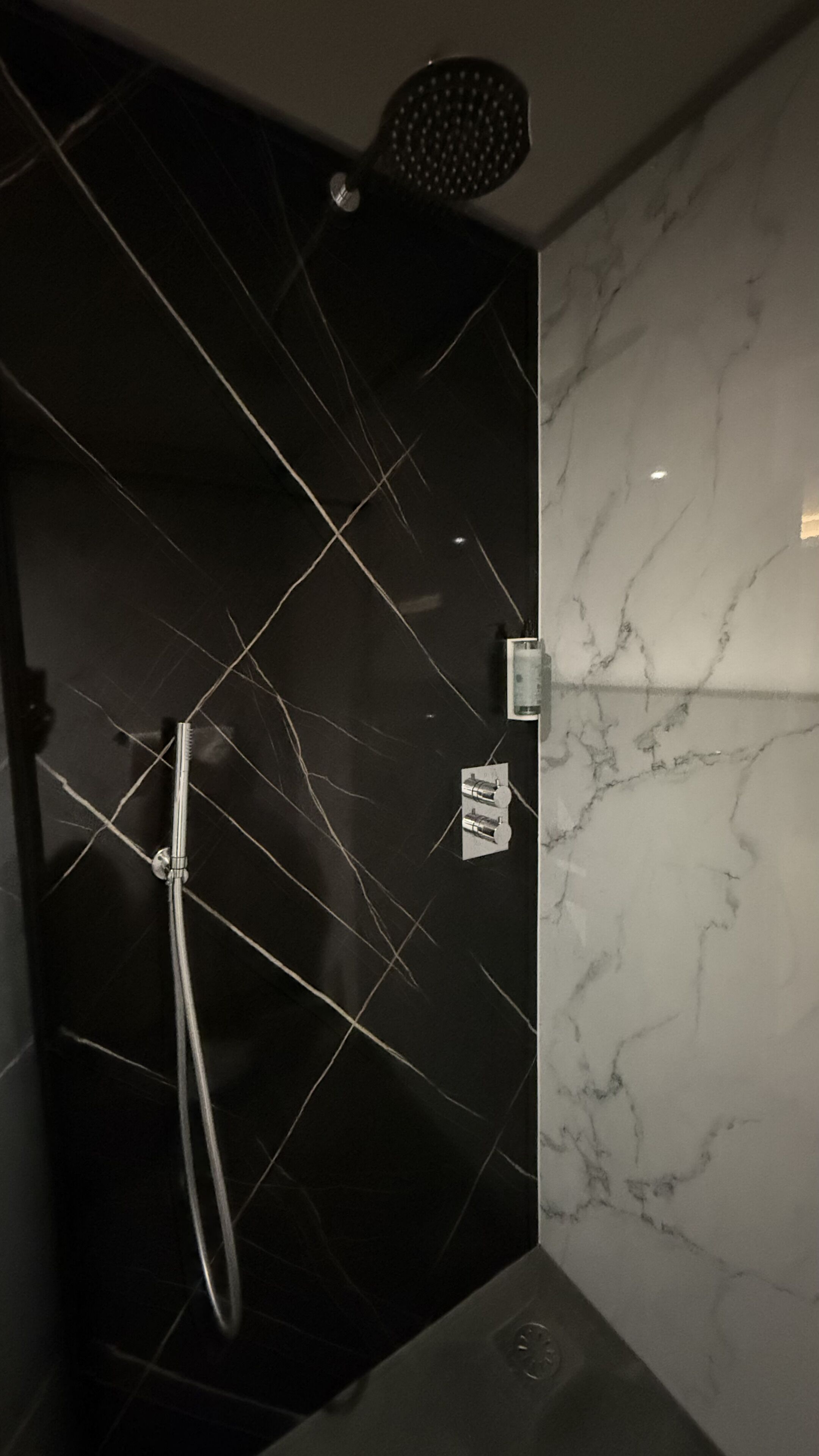 Un baño con pared de azulejos negros, cabezal de ducha y encimera de mármol.