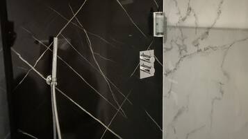 Un baño con pared de azulejos negros, cabezal de ducha y encimera de mármol.