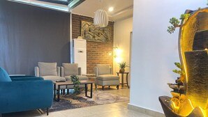 A modern living room with a blue sofa, two armchairs, a coffee table, and a fireplace. - Wallgate Apartments (Abuja)