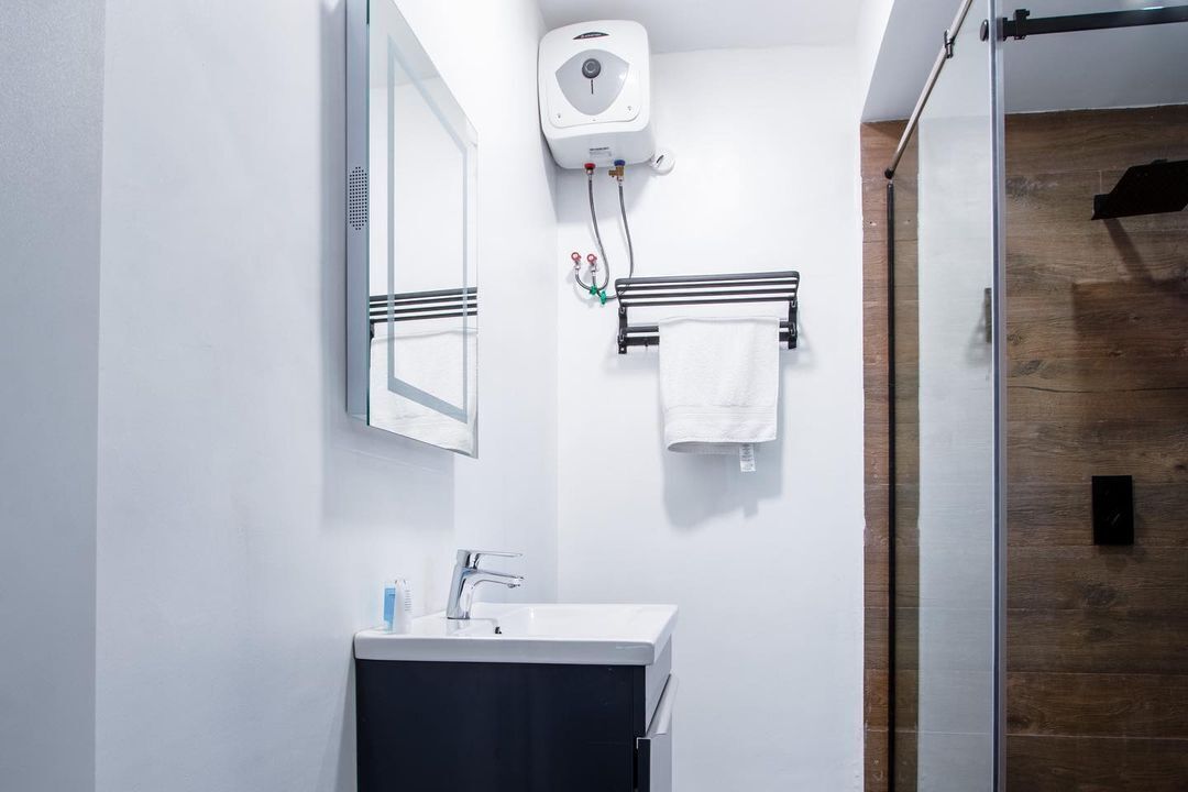 A modern bathroom with a white sink, mirror, towel rack, and a wall-mounted soap dispenser.