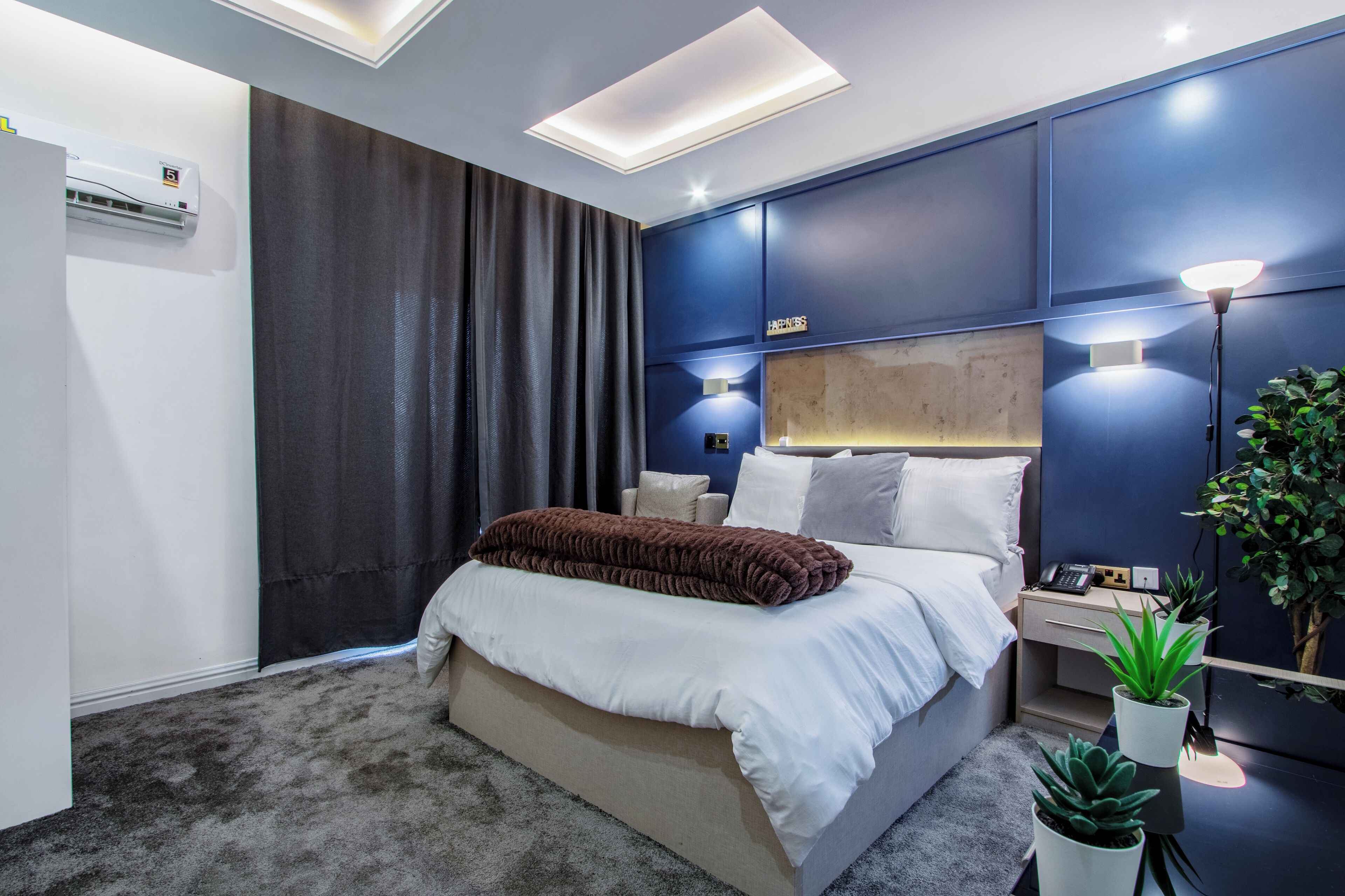 A modern bedroom with a large bed, bedside tables, a nightstand, and a wall-mounted air conditioner.