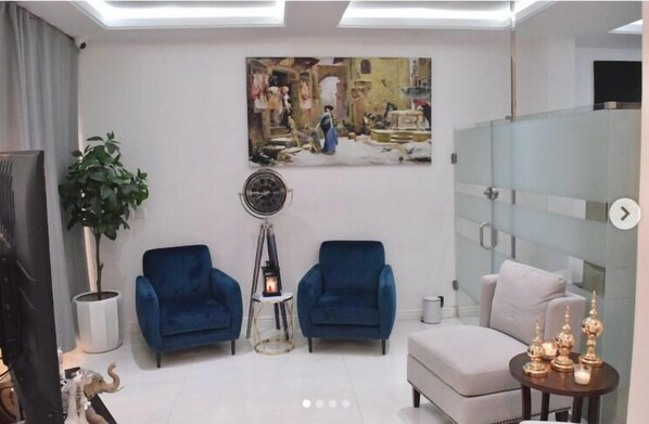 A modern living room with a large painting, two blue armchairs, a small side table with a lamp, and a white sofa. - Wallgate Apartments (Abuja)
