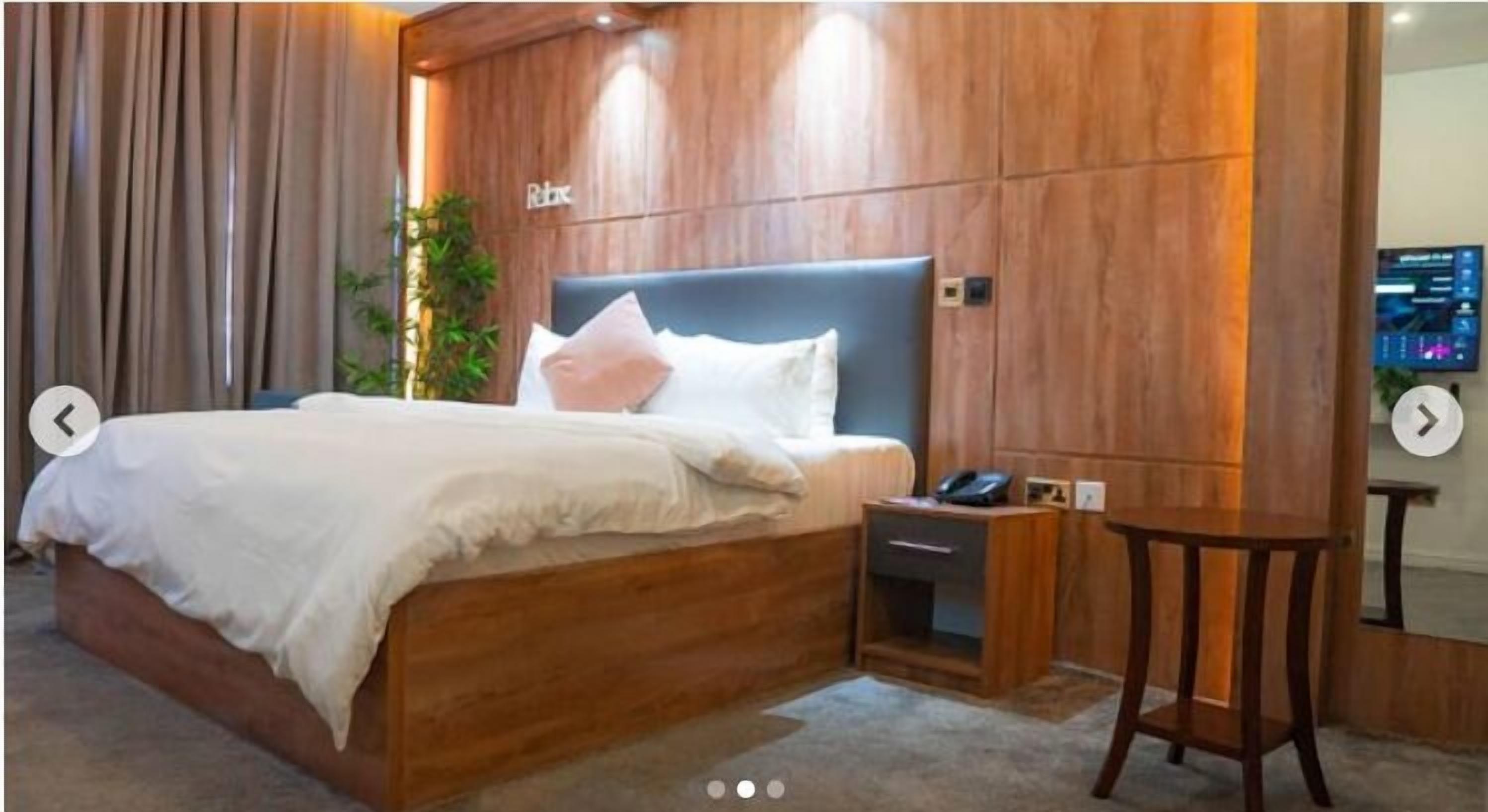 Ein Hotelzimmer mit Holz-Kopfteil, einem Bett mit weißer Bettwäsche, einem Nachttisch mit Telefon und einem kleinen Holztischchen.