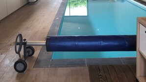 Une piscine intérieure moderne avec une vue dégagée sur l’extérieur, un plafond avec un revêtement en bois et un espace au bord de la piscine comprenant un fauteuil et une petite table.