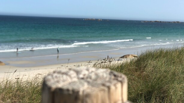 Une plage avec un poteau en bois au premier plan et une vue dégagée sur l’océan.