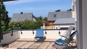 Une terrasse extérieure couverte, dotée d’une table et de chaises, d’un toit en verre et offrant une vue sur les maisons voisines.