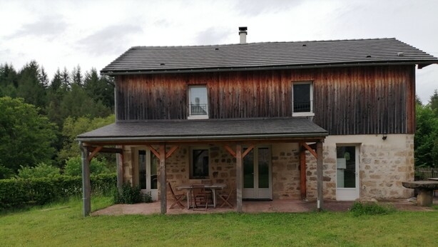 Ein zweistöckiges Holzhaus mit Steinanbau, einer Veranda und einem kleinen Garten.