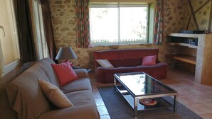 Ein Wohnzimmer mit einem beigen Sofa, einem roten Sessel, einem Glastisch und einer Steinwand.