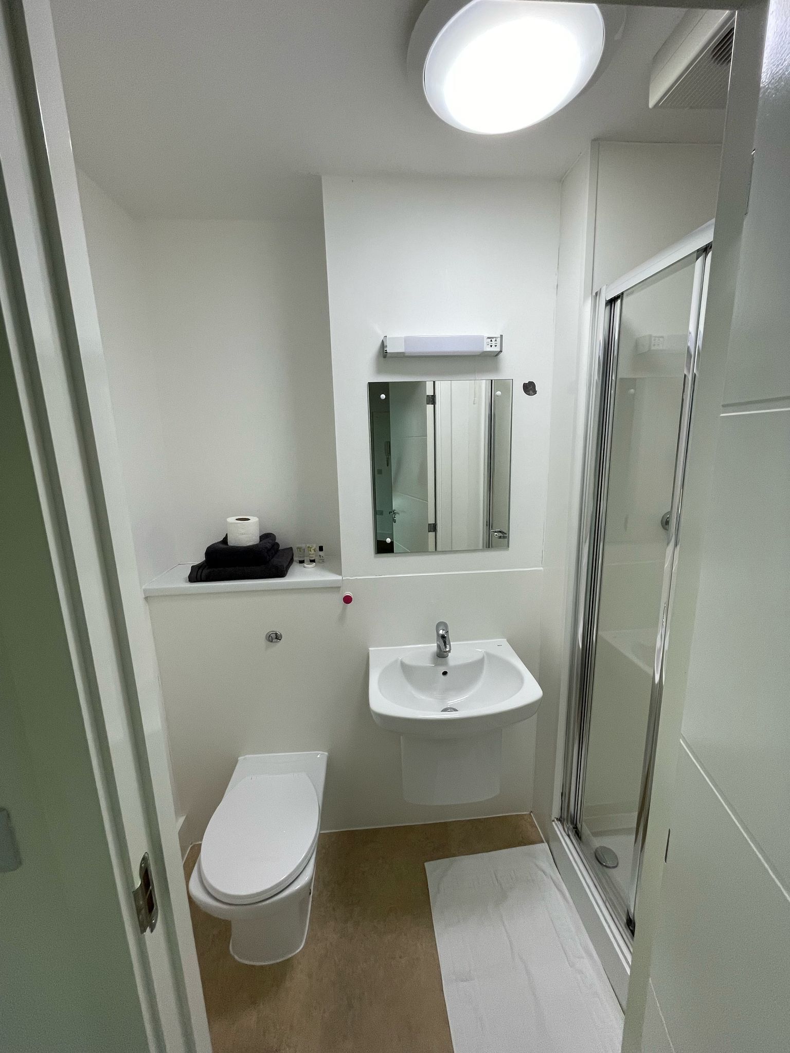 A small, clean bathroom with a toilet, sink, and glass shower stall.
