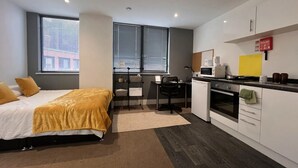 A compact bedroom with a bed, a desk, and a kitchenette.