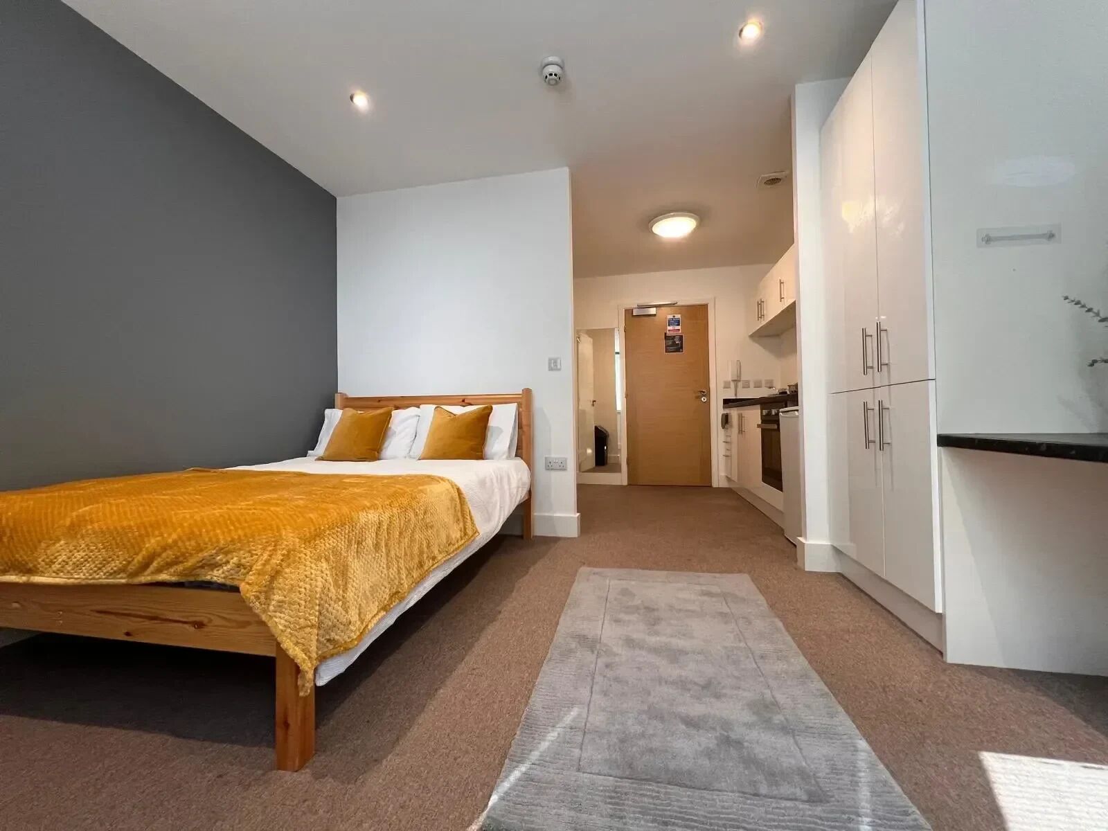 A modern bedroom with a wooden bed, a beige carpet, and white cabinets.