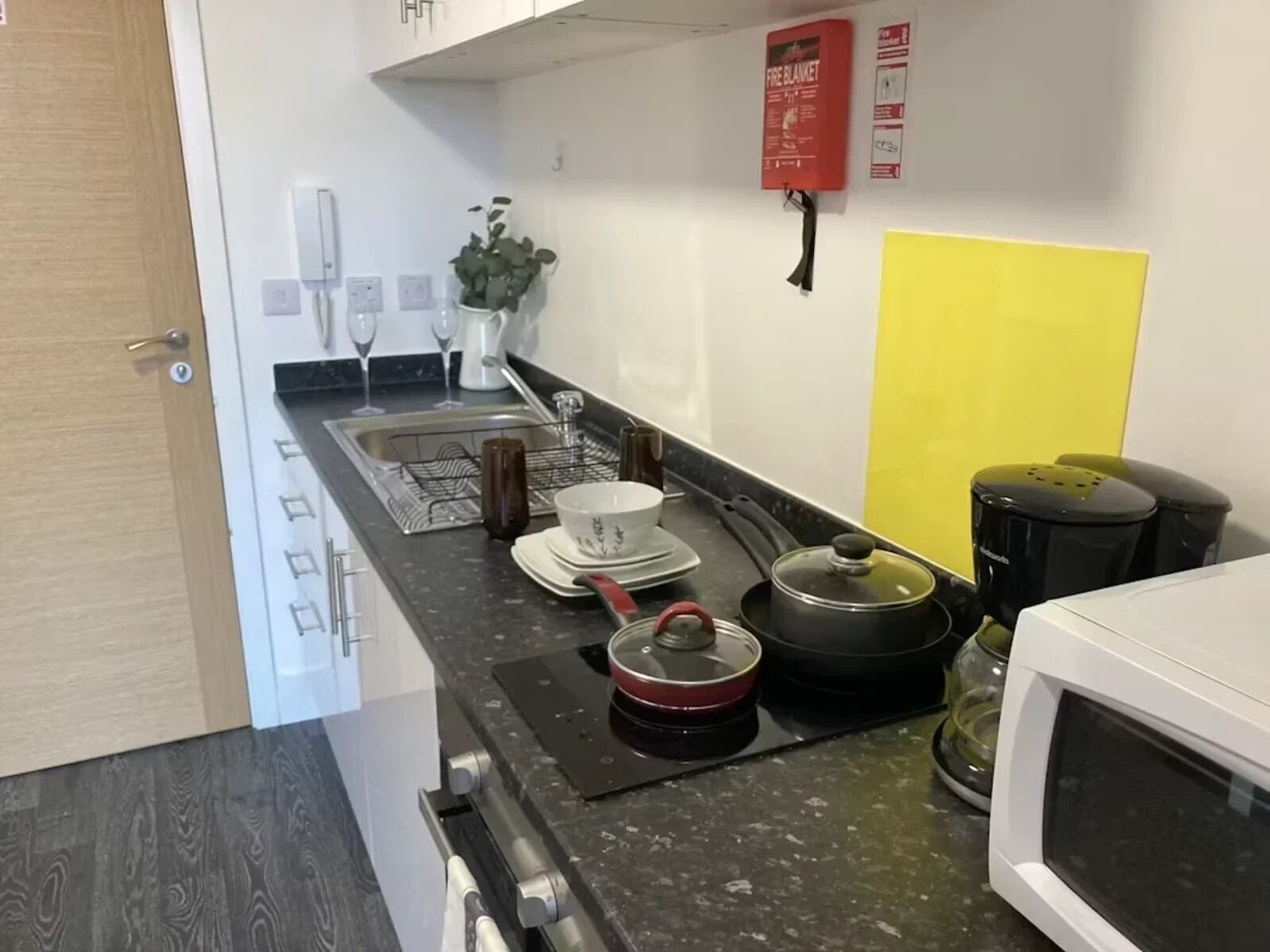 A compact kitchen with a microwave, kettle, and a coffee maker. A fire extinguisher is mounted on the wall.