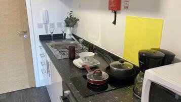 A compact kitchen with a microwave, kettle, and a coffee maker. A fire extinguisher is mounted on the wall.