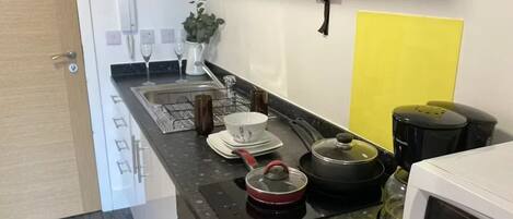 A compact kitchen with a microwave, kettle, and a coffee maker. A fire extinguisher is mounted on the wall.