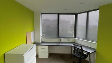 Quarto com escrivaninha, cadeira, penteadeira branca e janela com persianas.