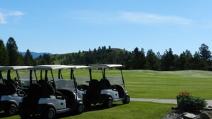 A row of golf carts parked on a golf course with a clear sky and a hilly landscape in the background.