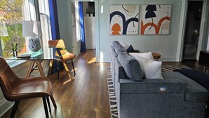 A modern living room with a grey sofa, a brown leather chair, a glass coffee table, and abstract wall art.
