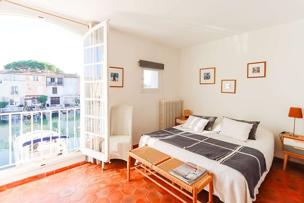 A bedroom with a bed, a chair, a table, and a view of a canal.