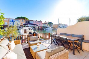 A patio with outdoor furniture, a table, and a view of boats and buildings in the background.