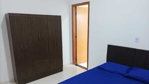A bedroom with a large wardrobe, a bed with blue bedding, and a door leading to another room. - Hospedagem Mobiliada (Tupa)