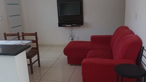 A living room with a red sofa, a wooden chair, a small table, and a TV mounted on the wall. - Hospedagem Mobiliada (Tupa)