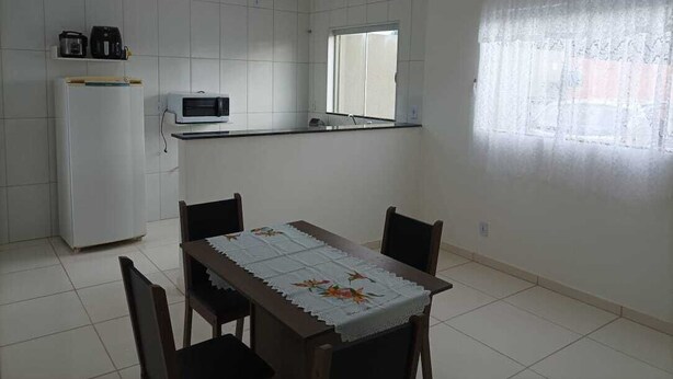A kitchen with white tiles, a refrigerator, a microwave, a coffee maker, and a window with a curtain. - Hospedagem Mobiliada (Tupa)