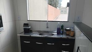 A small kitchen with a sink, two chairs, and a window. - Hospedagem Mobiliada (Tupa)