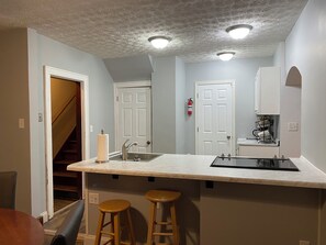 A kitchen with a marble countertop, two wooden stools, a stainless steel sink, and a white door with a fire extinguisher.
