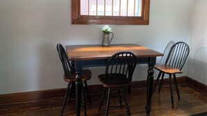 Un comedor con una mesa de madera y cuatro sillas. Encima de la mesa, hay un florero con flores y una ventana con marco de madera.