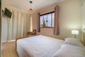 Quarto com cama grande, televisão na parede e janela com cortinas.