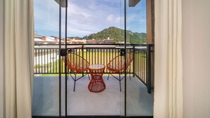 Varanda com duas cadeiras de vime e uma mesa pequena, com vista para uma encosta verde e edifícios.
