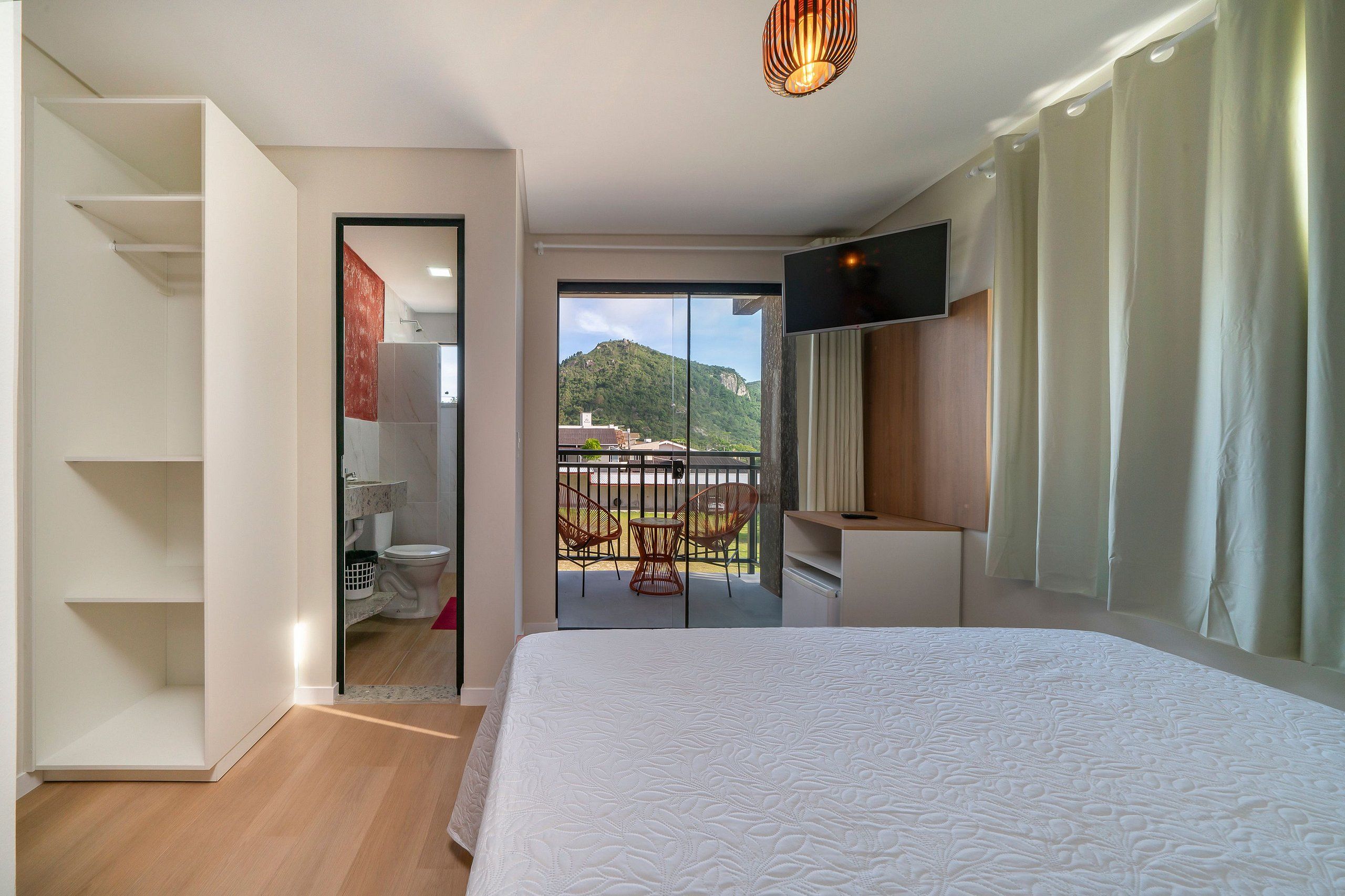 A hotel room with a bed, a TV, a balcony with chairs, and a view of a mountain.