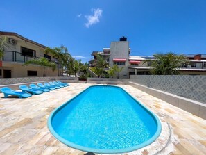 Piscina com espreguiçadeiras, cercada por edifícios e palmeiras.