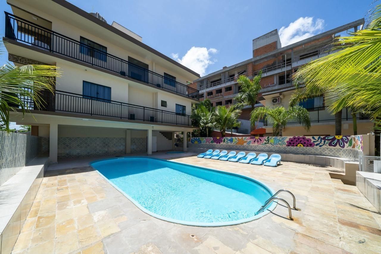 Una piscina con sillones de descanso, un área techada y un edificio de varios pisos con balcones.