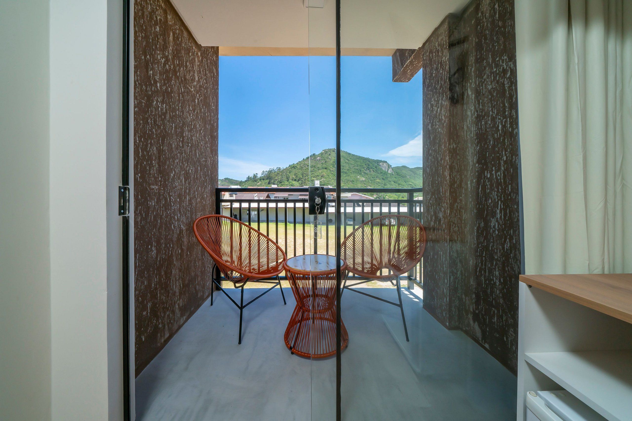 A balcony with a table and two chairs, a view of a mountain, and a person in the distance.
