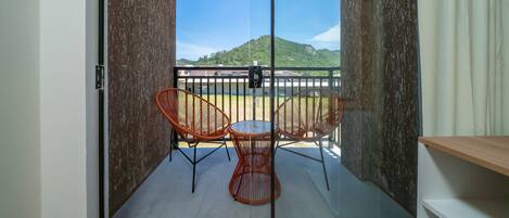 A balcony with a table and two chairs, a view of a mountain, and a person in the distance.