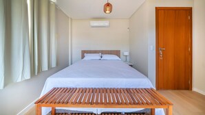 Quarto com cama, mesa de madeira, ar condicionado, porta e luminária suspensa.